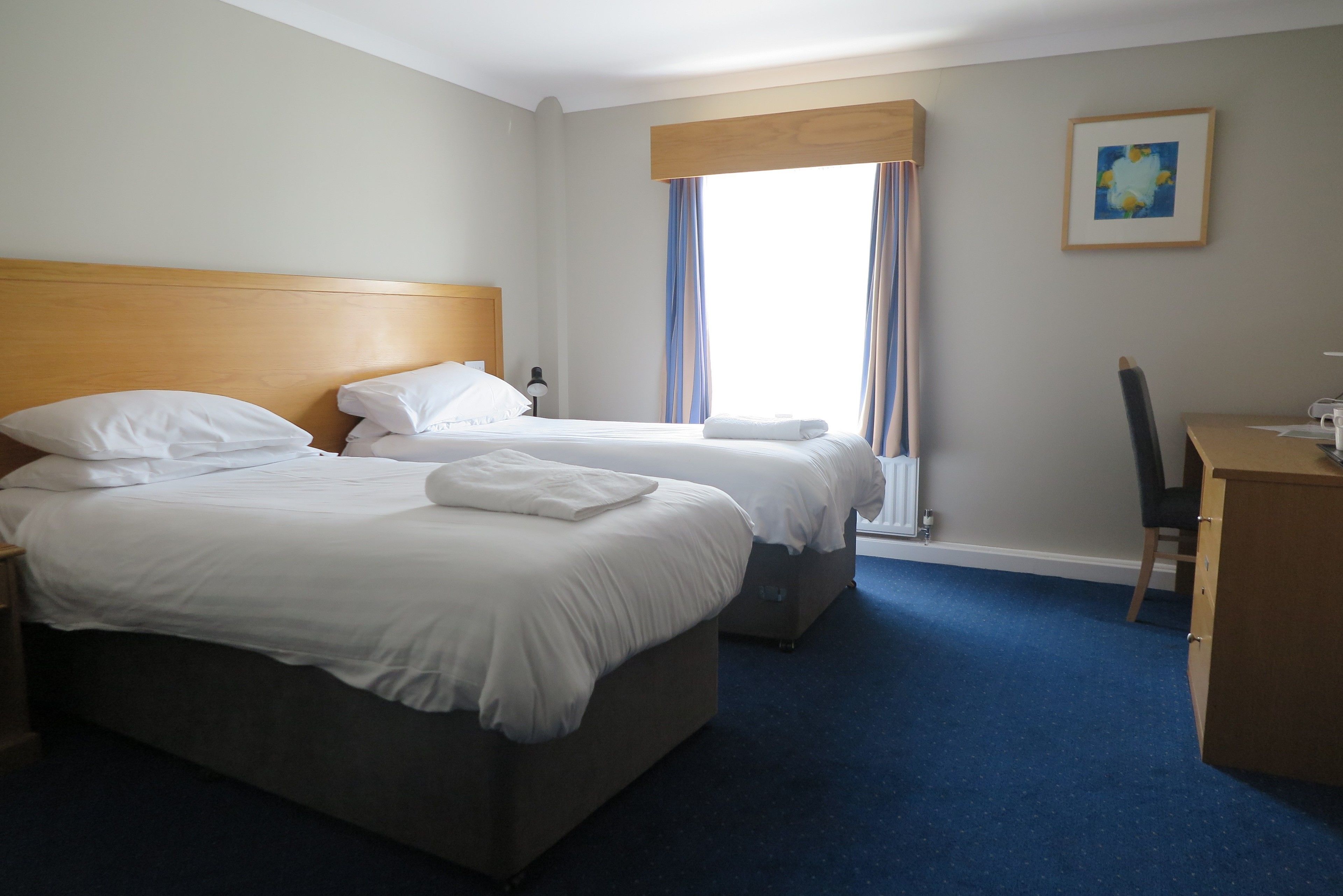 A hotel room with two beds, a wooden headboard, a desk, and a chair.