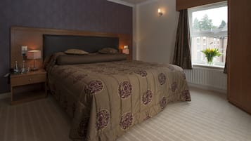 A bedroom with a large bed, a nightstand with a lamp, a window with a view of buildings, and a wall with a patterned design.