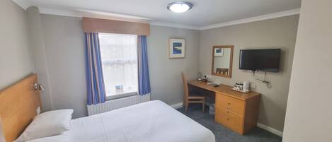 A hotel room with a bed, a desk, a chair, a TV, and a window with curtains.