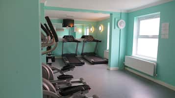 Un gimnasio con cintas de correr, bicicletas estáticas y un espejo grande.