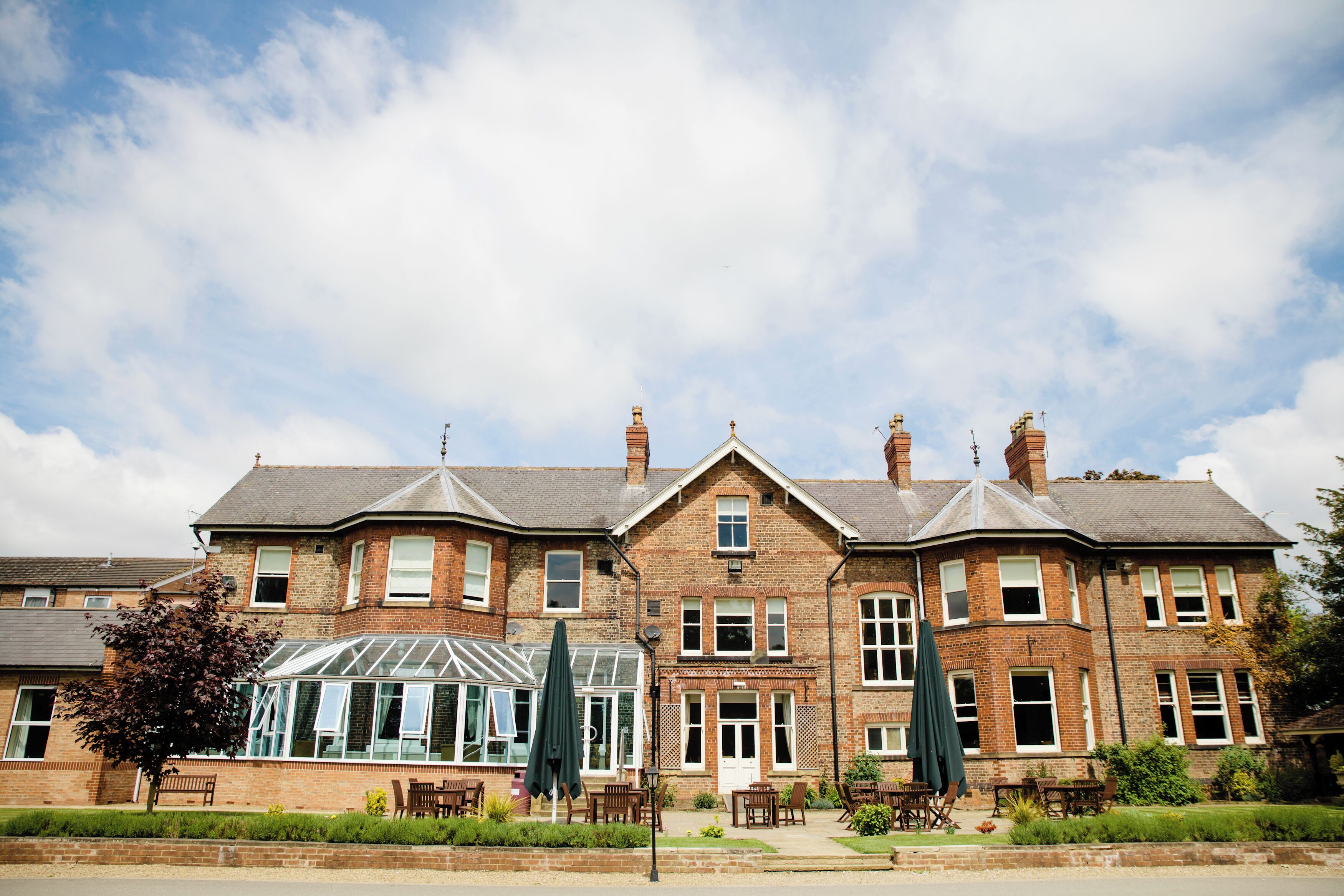 A large brick house with a conservatory, multiple windows, and outdoor seating.