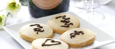 A plate of cookies with chocolate drizzle, a bottle of champagne, and a glass of wine on a table.
