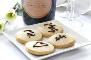 A plate of cookies with chocolate drizzle, a bottle of champagne, and a glass of wine on a table. - Burn Hall Hotel (York)