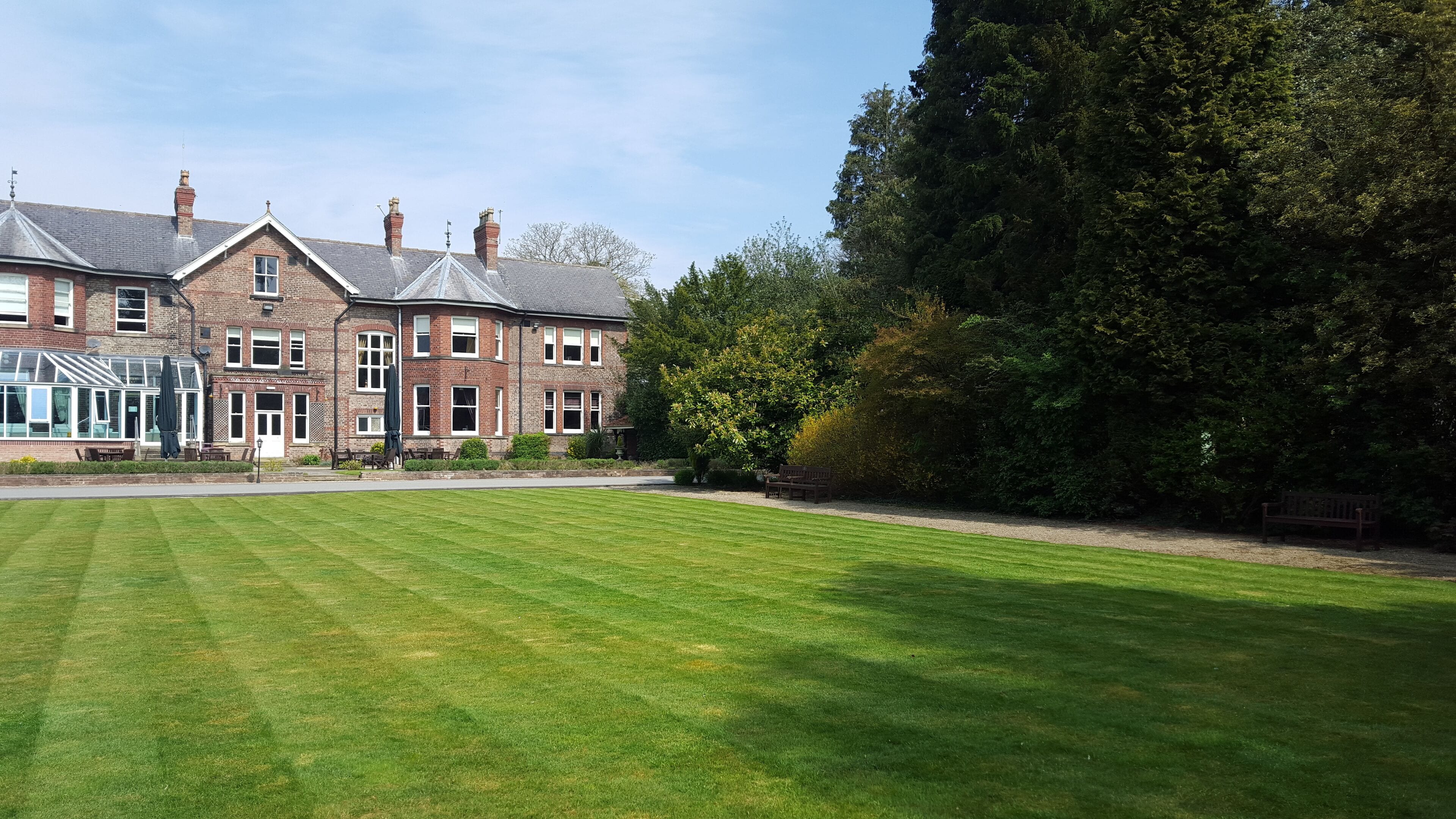 A large, multi-story brick building with a well-maintained lawn and a conservatory.