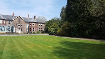 A large, multi-story brick building with a well-maintained lawn and a conservatory.