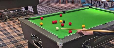 A pool table with balls in a room with checkered flooring and chairs around a table.