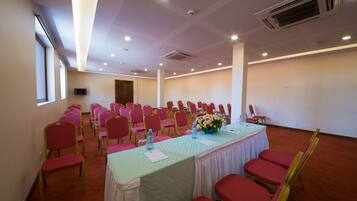 A conference room with rows of red chairs, a table with a checkered tablecloth, and a vase of flowers.