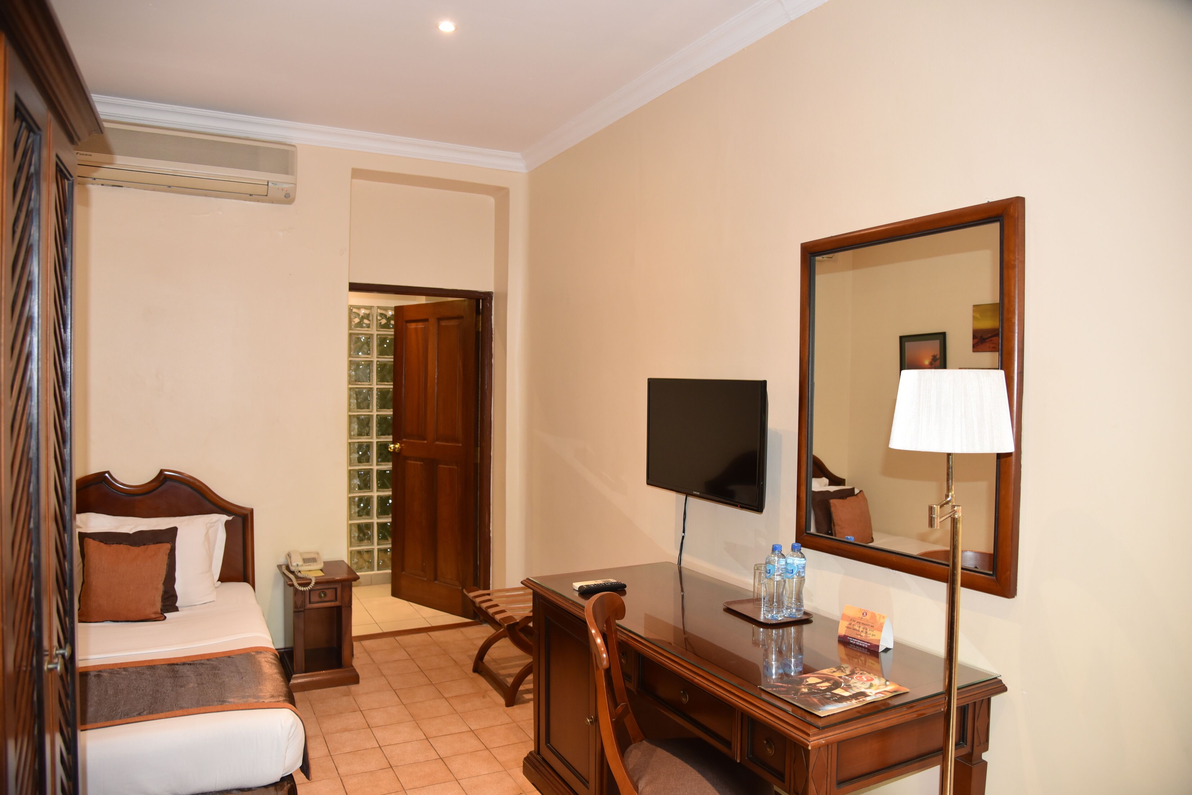 A hotel room with a bed, bedside table, desk, chair, and a large mirror.