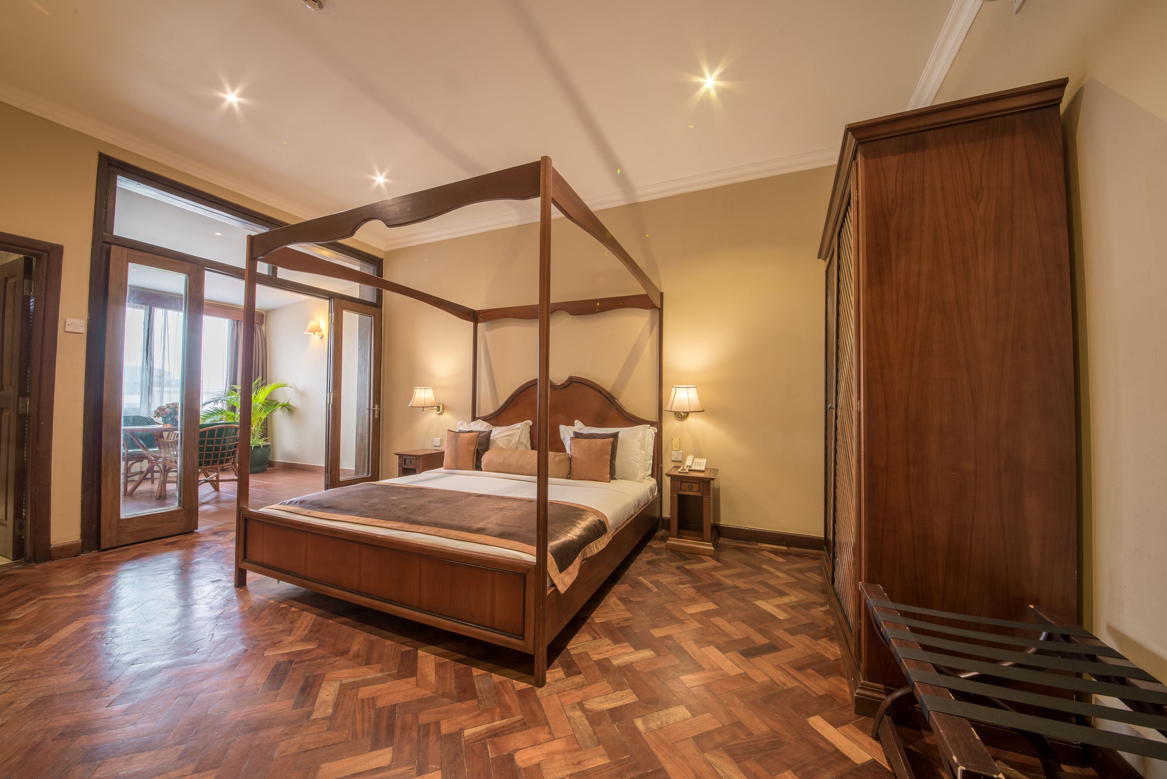 A four-poster bed with a wooden frame and a matching headboard, a wooden bench, and a large wooden wardrobe.