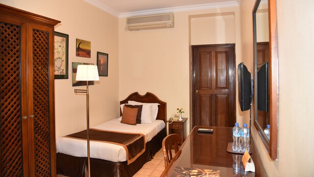 A hotel room with two beds, a desk with a chair, a mirror, a wall-mounted TV, and a door. - Speke Hotel (Kampala)