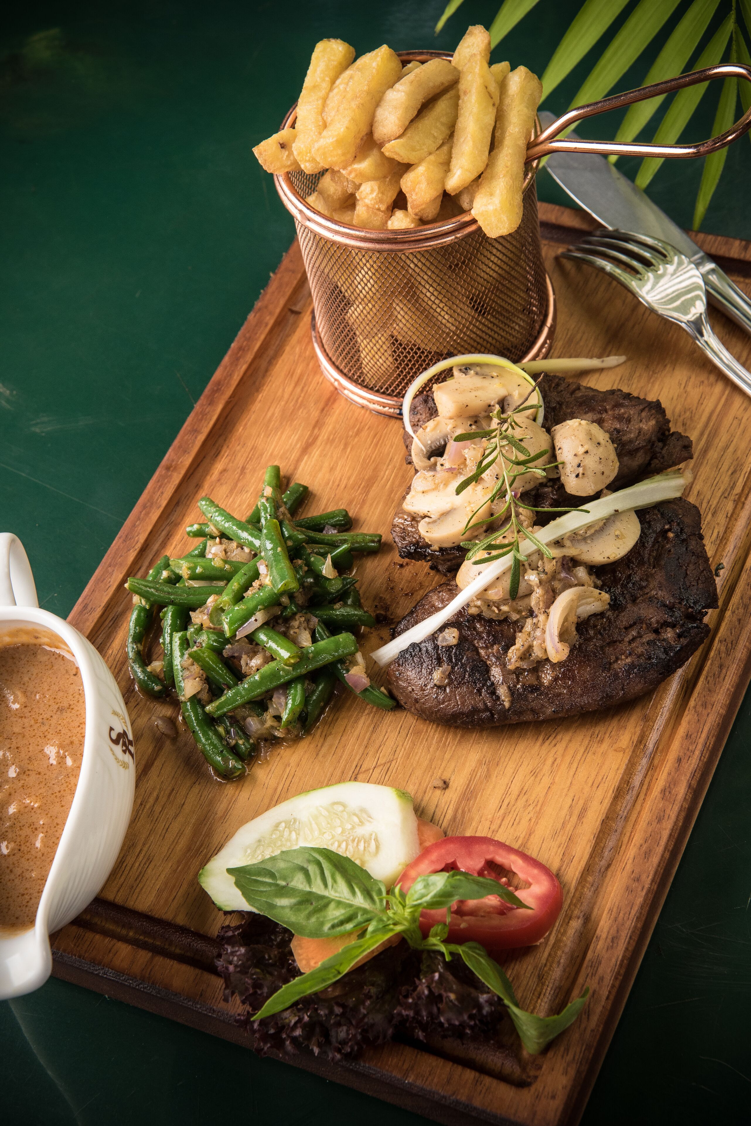 A meal with a steak, green beans, mushrooms, and fries on a wooden board.