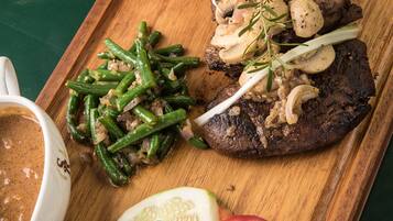 A meal with a steak, green beans, mushrooms, and fries on a wooden board.