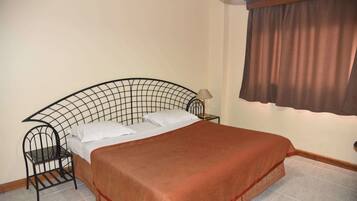 A neatly made bed with a headboard, a small bedside table with a lamp, and a window with curtains.
