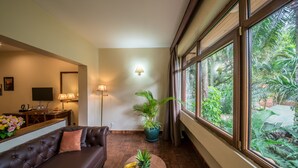 Un salón con un sofá de cuero marrón, una mesa de centro de madera con frutas, una planta en maceta y un ventanal con vistas al verdor.