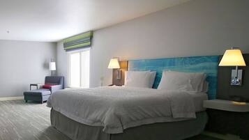 A hotel room with a large bed, two bedside lamps, a small table, a chair, and a window.