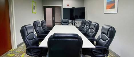 A conference room with a long table and eight black leather chairs, a flat-screen TV, and framed artwork on the walls.