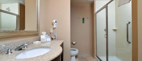 Un baño con lavamanos, espejo, secador de pelo, inodoro y zona de ducha con mampara de vidrio.