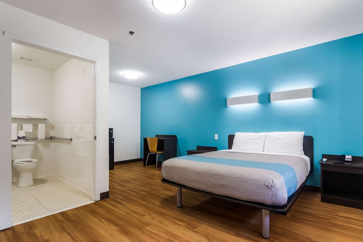 Une chambre d’hôtel comprenant un lit, un bureau, une chaise, une salle de bain et un mur d’accent bleu.