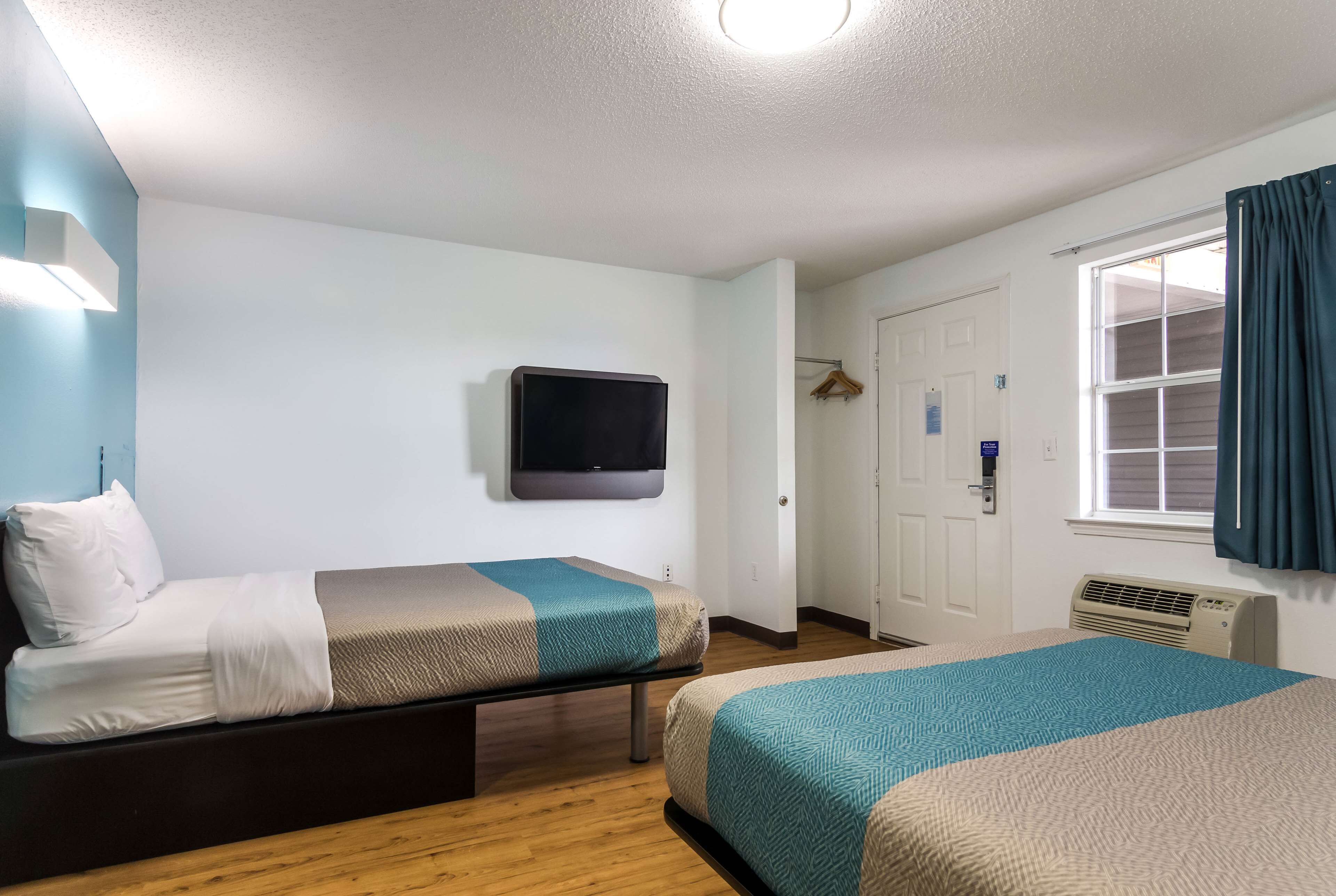 Habitación de hotel con dos camas, televisión, calefacción y ventana con cortinas.