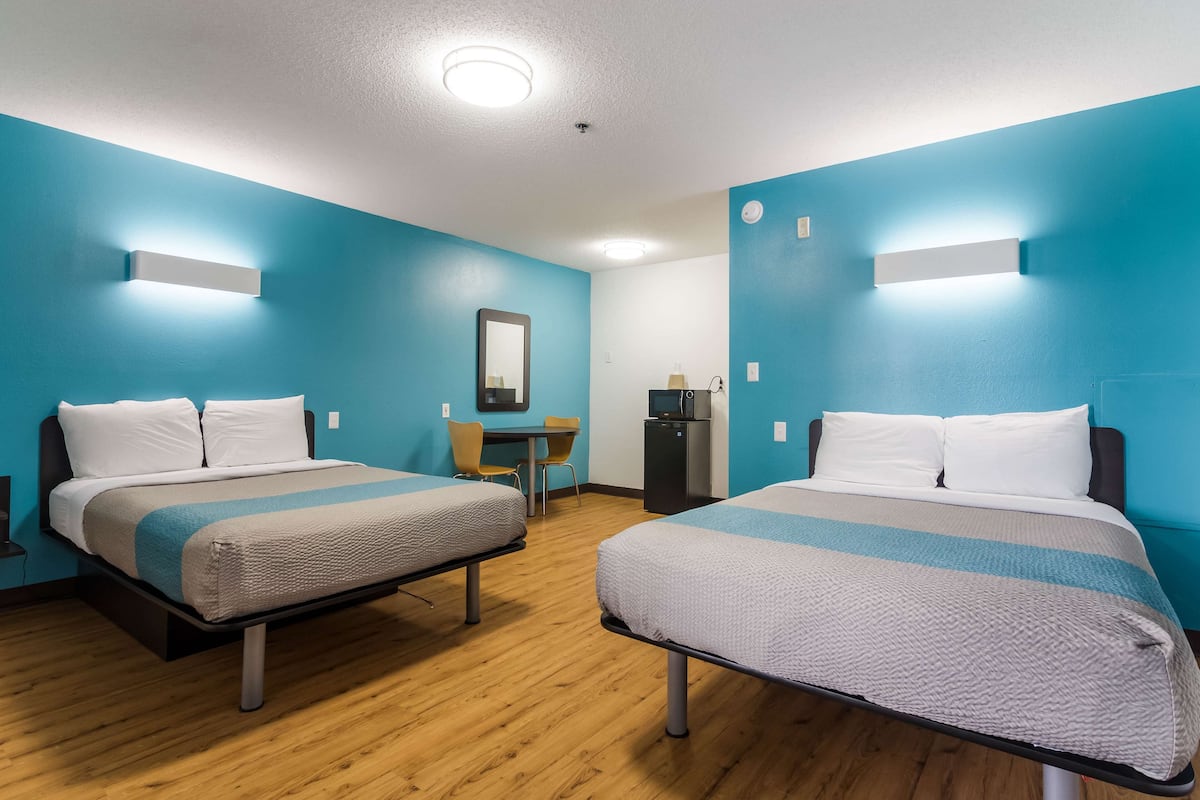 Une chambre d’hôtel avec deux lits, un bureau, une chaise et un réfrigérateur.