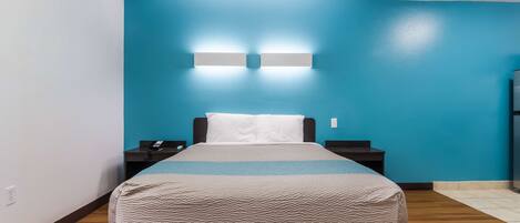 A hotel room with a bed, nightstands, a blue wall, and a wooden floor.