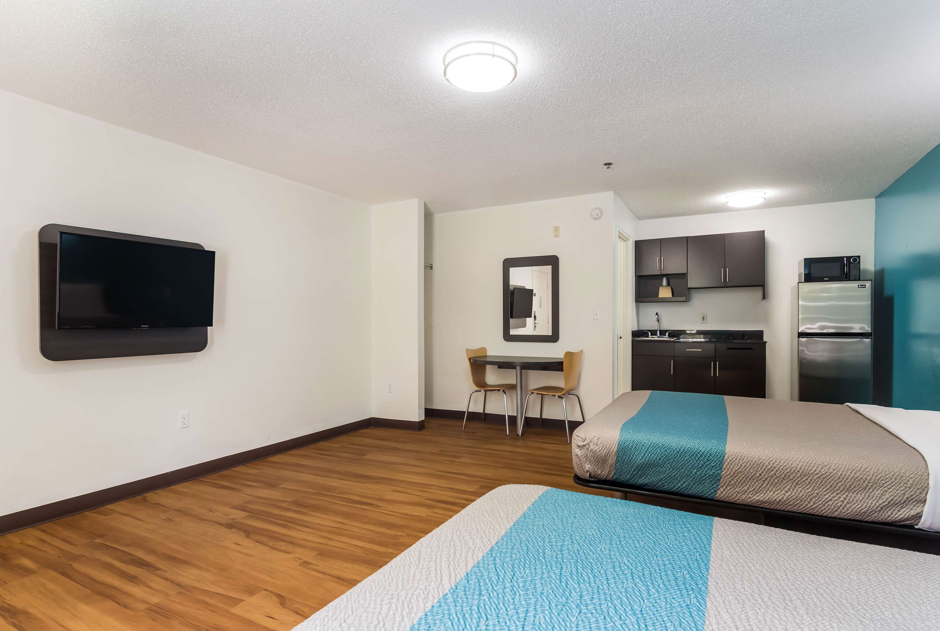 A hotel room with two beds, a TV, a small kitchenette, and a dining area.