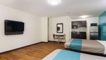 A hotel room with two beds, a TV, a small kitchenette, and a dining area.