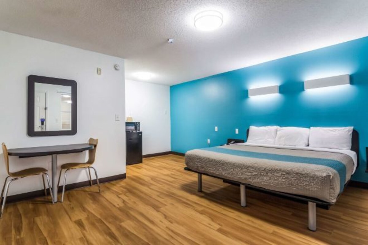 Hotelkamer met een bed, bureau, twee stoelen, spiegel en een blauwe accentmuur.