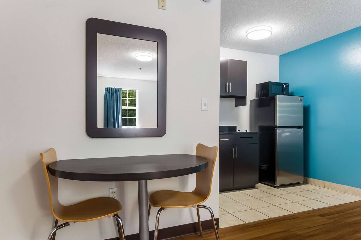 Une cuisine compacte dotée d’appareils électroménagers modernes, un coin repas avec deux chaises et un miroir au mur.