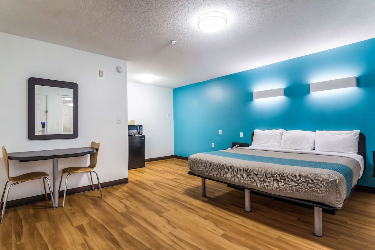 Une chambre d’hôtel avec un lit, un bureau avec des chaises, un miroir et un mur d’accent bleu.