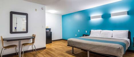 A hotel room with a bed, a desk with chairs, a mirror, and a blue accent wall.