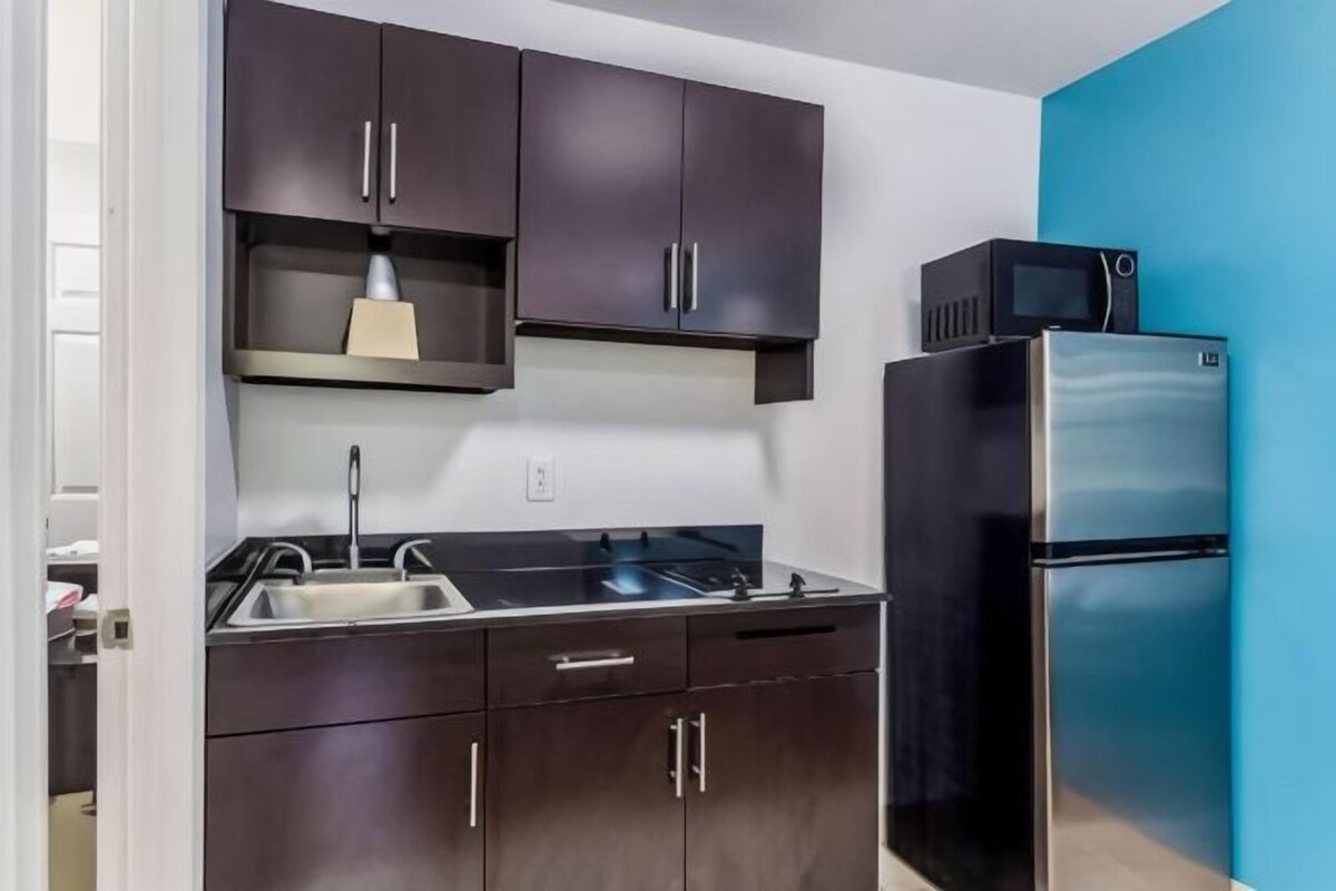 Una cocina moderna con gabinetes oscuros, un lavamanos de acero inoxidable y un refrigerador negro.