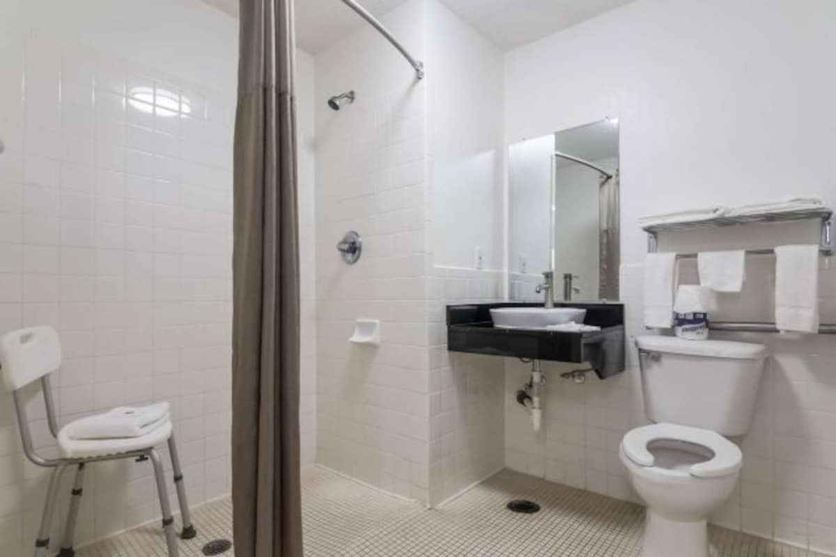 A bathroom with a shower, toilet, sink, and a chair.