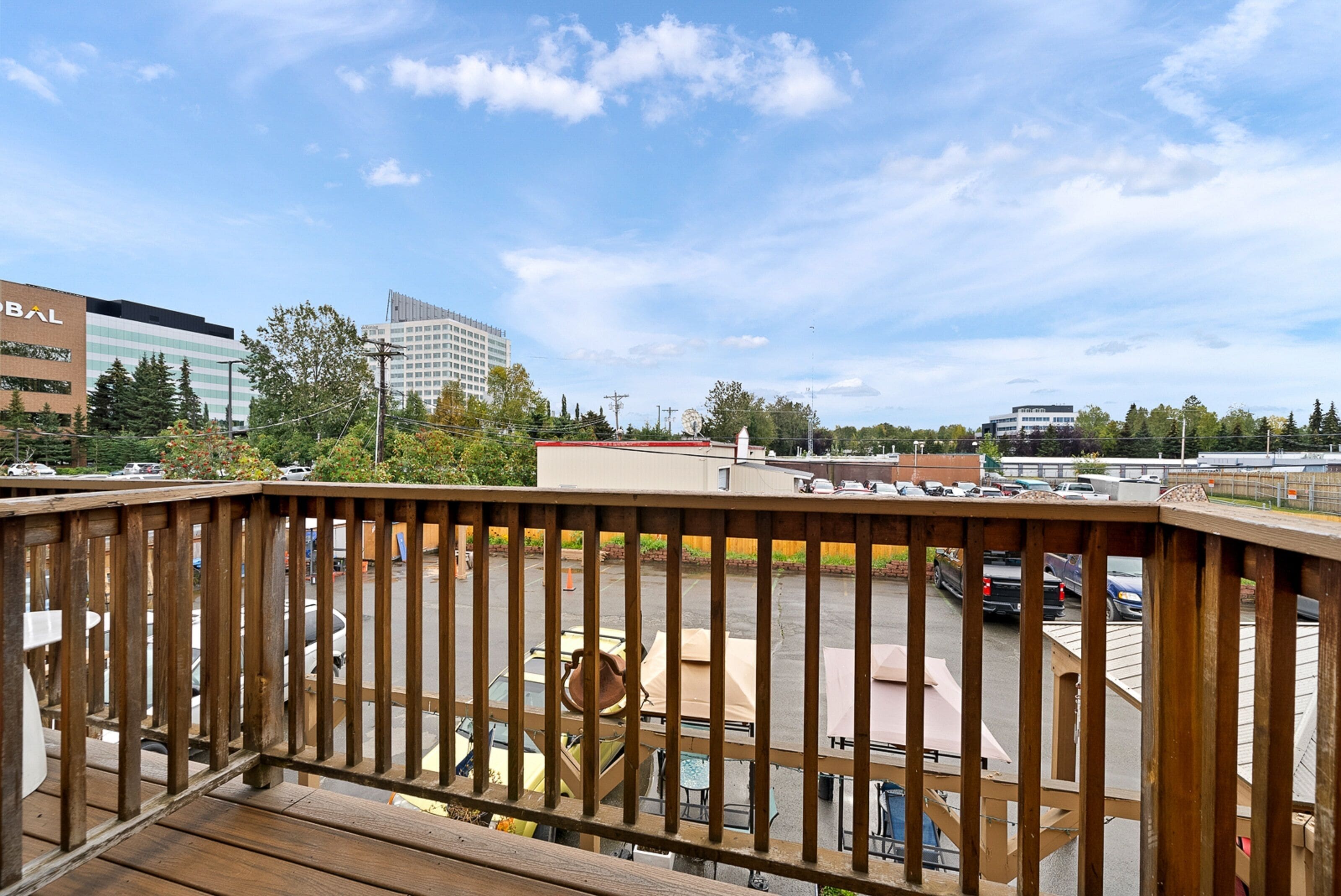 Een houten terras met uitzicht op een parkeerplaats en gebouwen op de achtergrond.