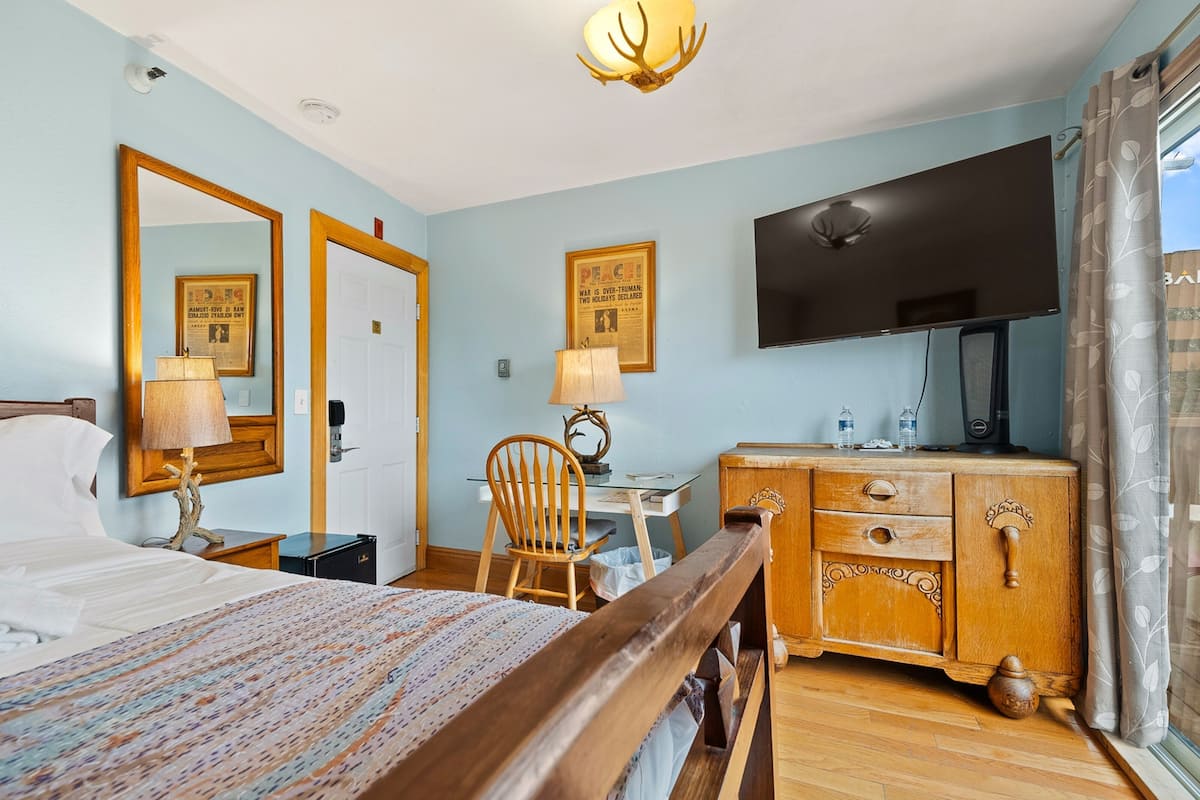 Habitación de hotel con una cama, un escritorio, una silla, un aparador, un televisor y un espejo.
