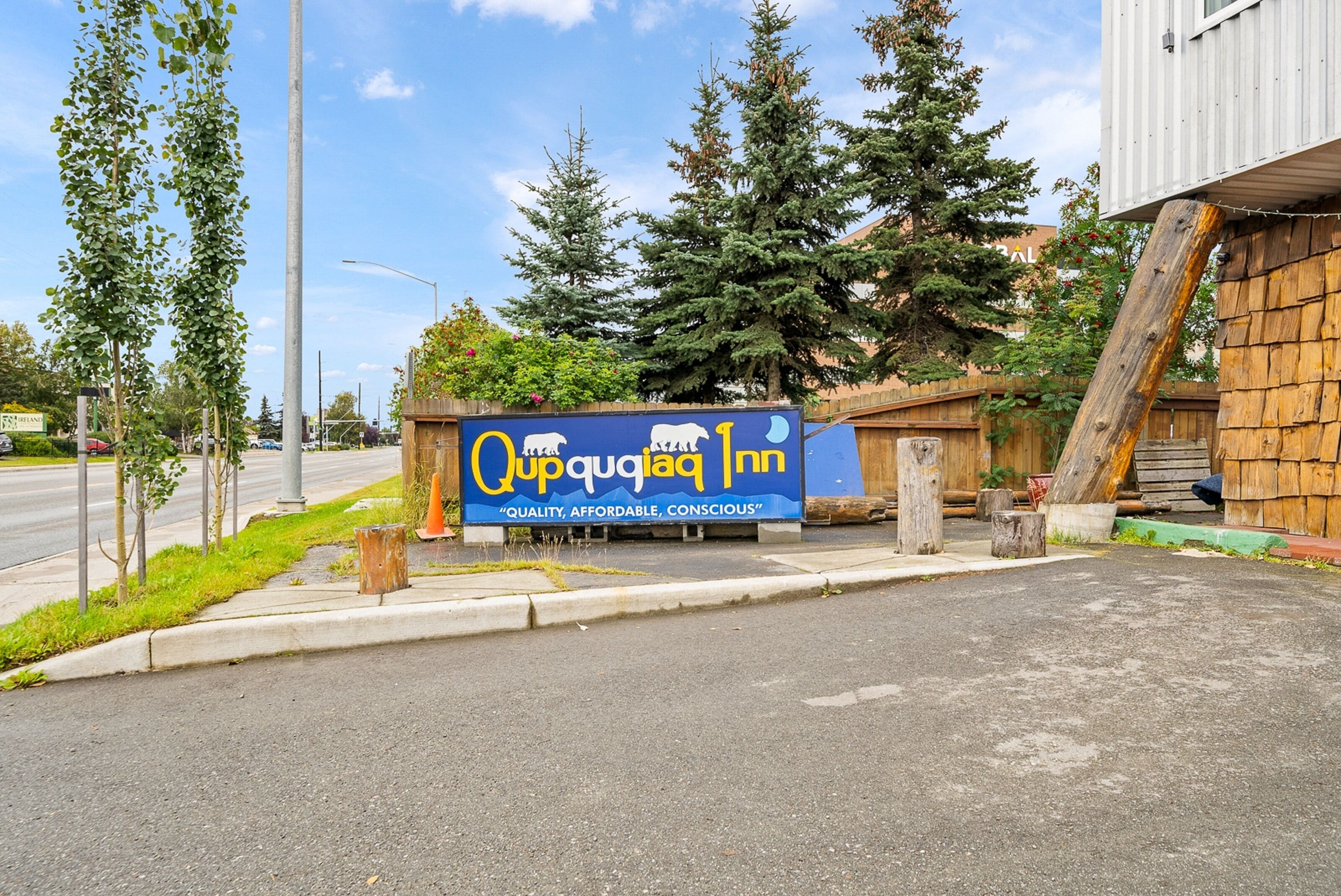 A sign for the Qupqiaq Inn with a clear view of the surrounding area, including trees and a building structure.