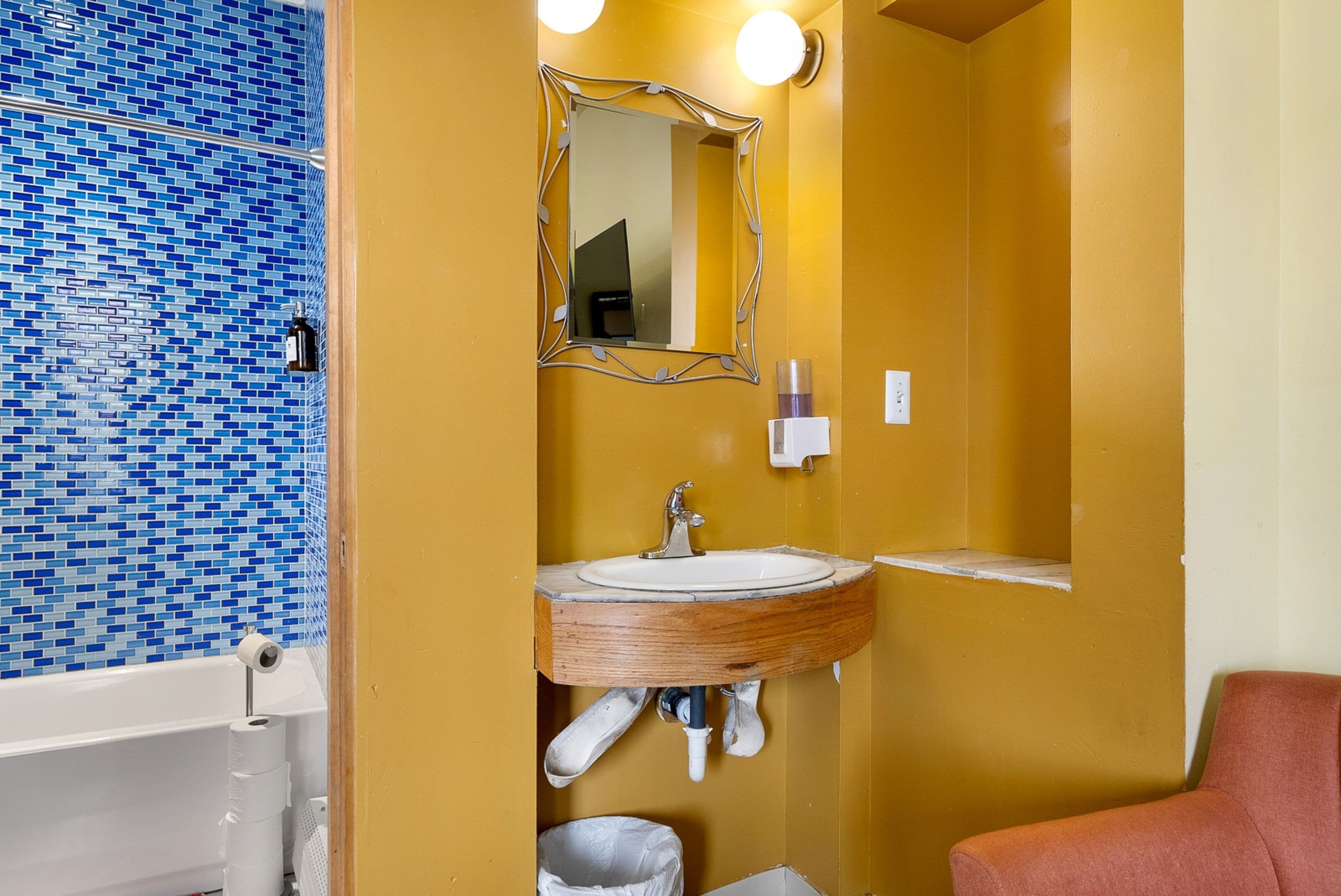 A bathroom with a blue mosaic tile wall, a wooden vanity with a mirror, and a white sink.
