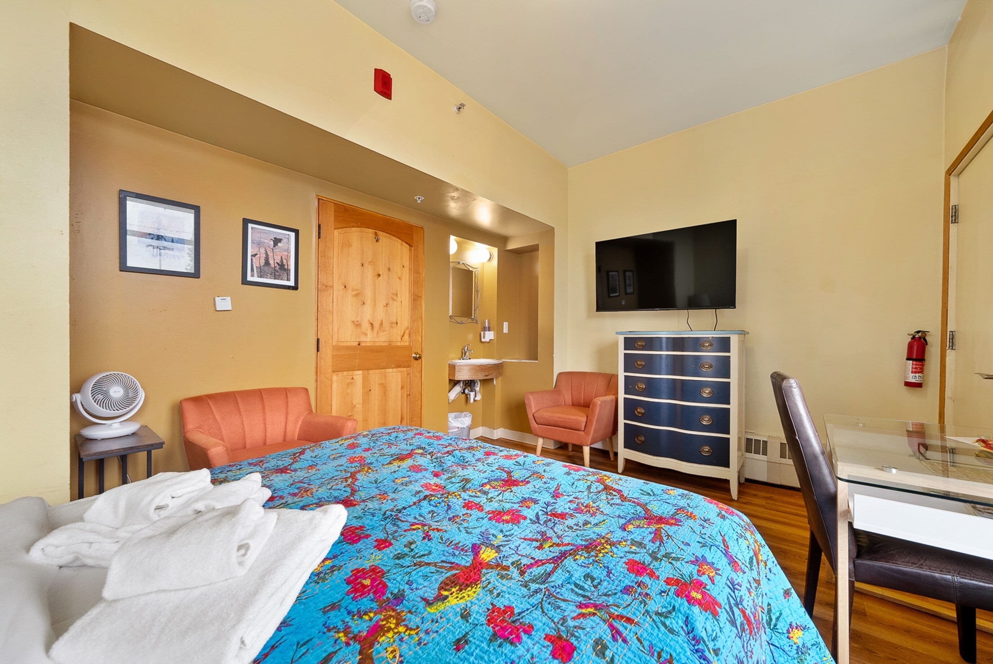 A hotel room with a bed, a dresser, a television, and a desk with a chair.