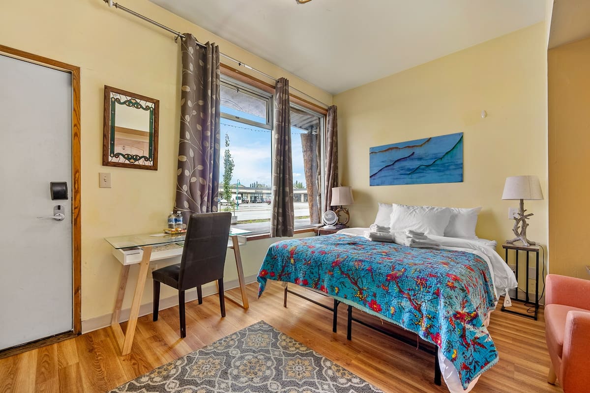 Habitación de hotel con cama, escritorio, silla y vistas al exterior.