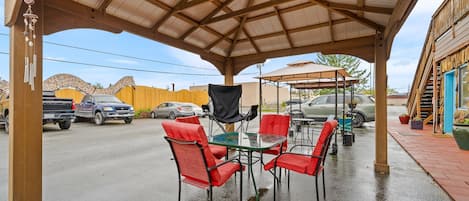 A covered outdoor seating area with a table and chairs, a wooden pergola, and a view of a street with parked cars.