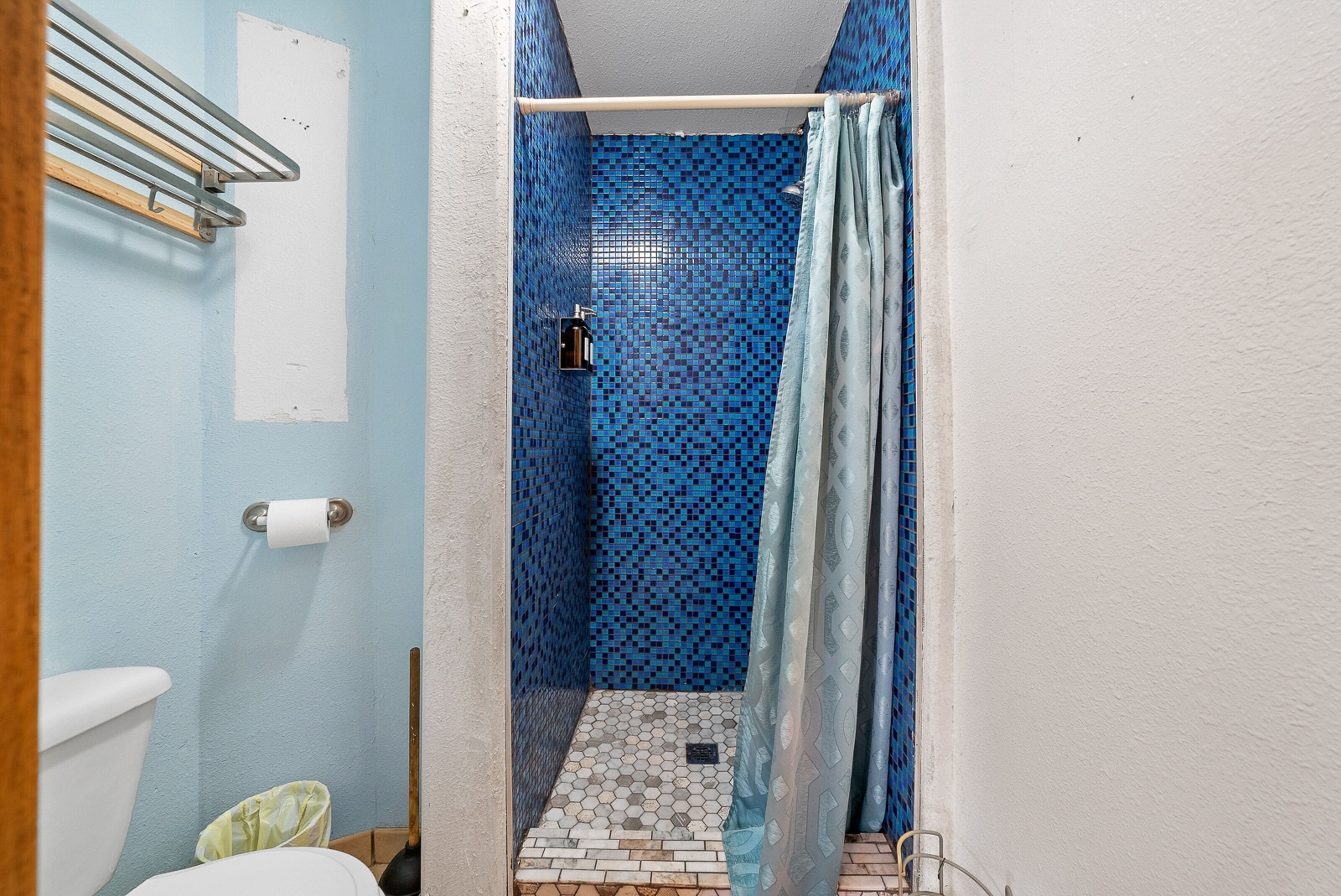 Un baño estrecho con una zona de ducha azulejada en azul, un inodoro blanco y un dispensador de papel higiénico a la vista.
