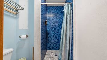 Un baño estrecho con una zona de ducha azulejada en azul, un inodoro blanco y un dispensador de papel higiénico a la vista.