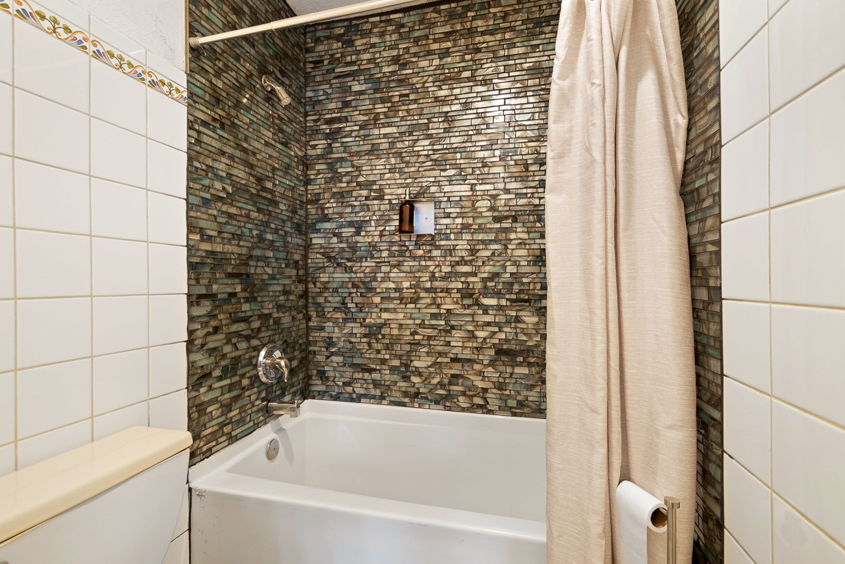 A bathroom with a bathtub, a shower curtain, and a tiled wall with a mosaic pattern.