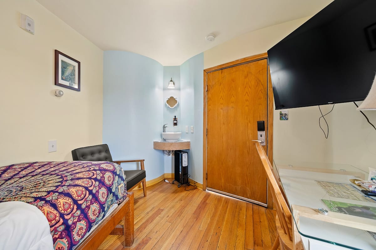 Un dormitorio con cama, una silla, un armario de madera, un lavamanos y un televisor.