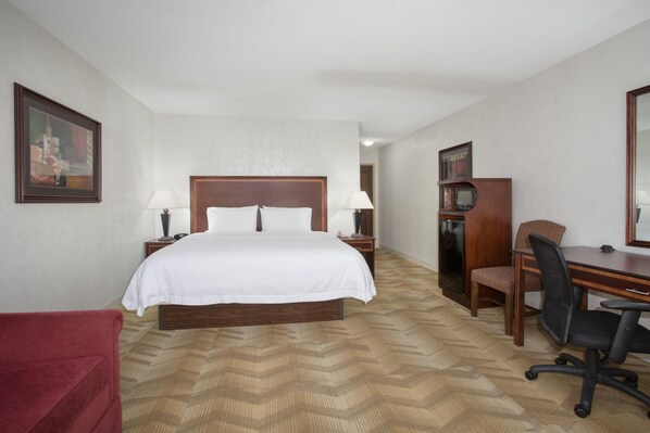 A hotel room with a bed, bedside lamps, a desk with a chair, a television, and a red chair. - Hampton Inn Siloam Springs (Siloam Springs)