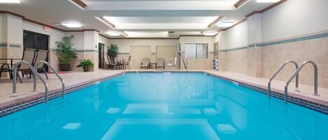 A swimming pool with chairs and tables, a staircase, and a ceiling with recessed lighting.