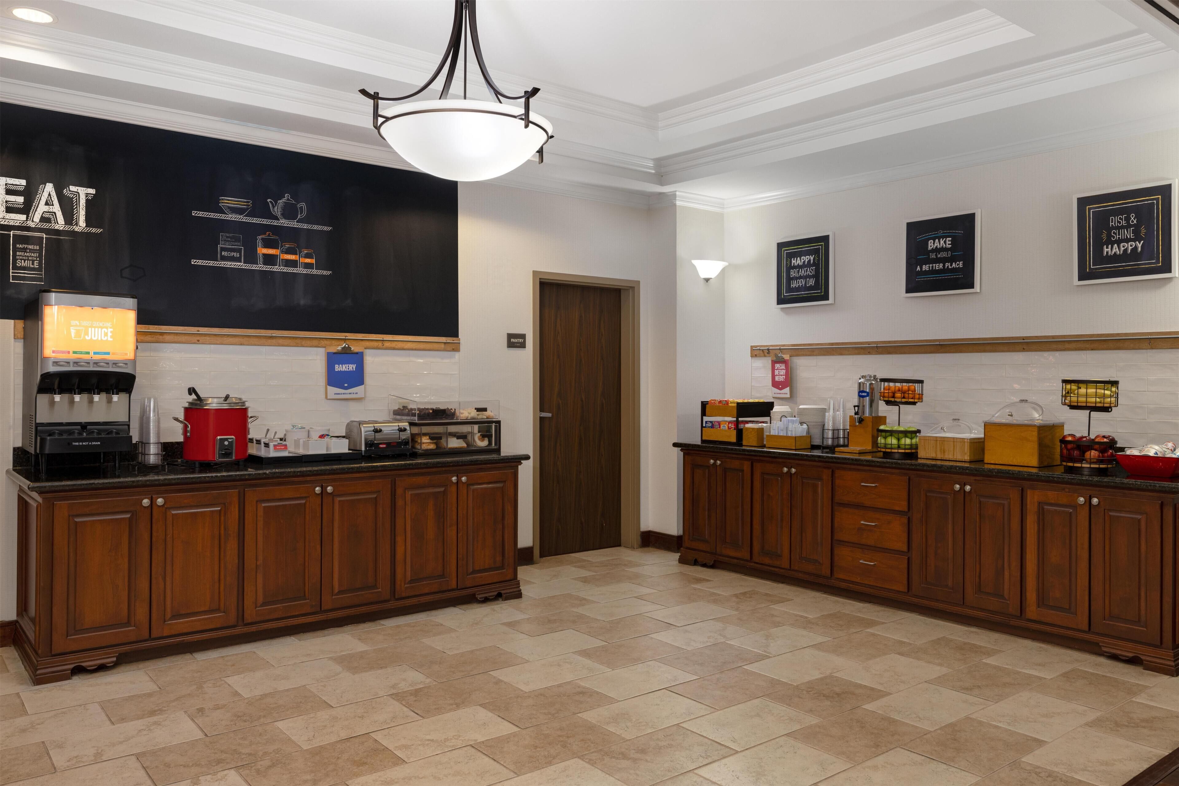 A kitchen with wooden cabinets, a coffee machine, and a chalkboard with menu items.