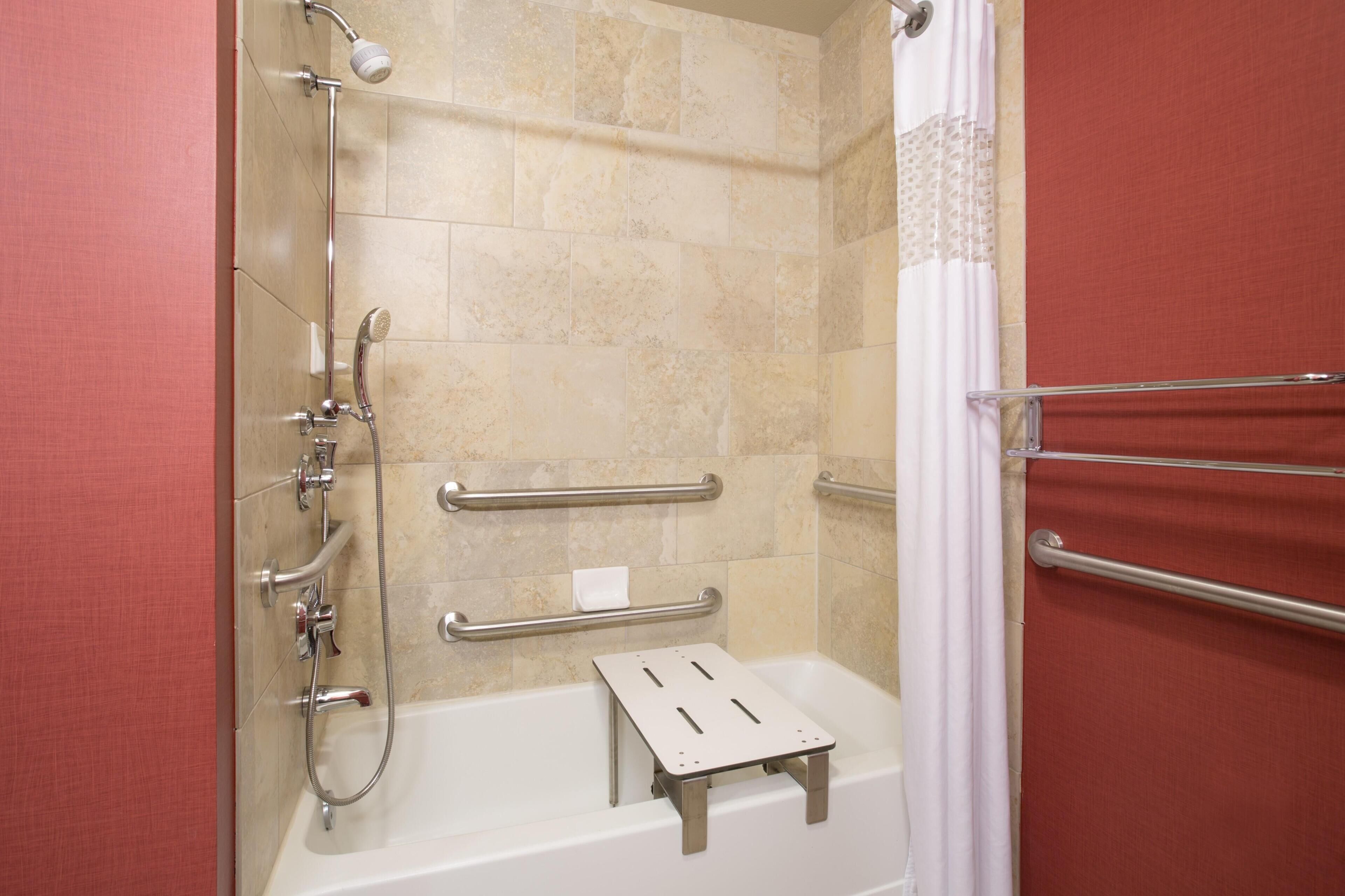 A shower area with a handheld showerhead, a handheld shower attachment, a handheld shower hose, a grab bar, and a step for accessibility.