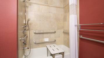 A shower area with a handheld showerhead, a handheld shower attachment, a handheld shower hose, a grab bar, and a step for accessibility.