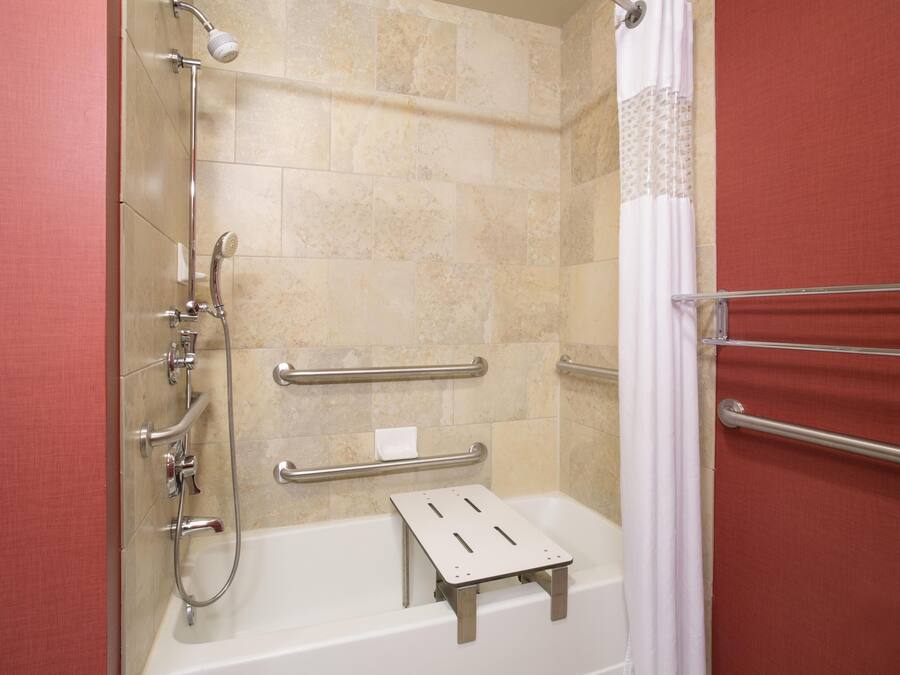 A shower area with a handheld showerhead, a handheld shower attachment, a handheld shower hose, a grab bar, and a step for accessibility.